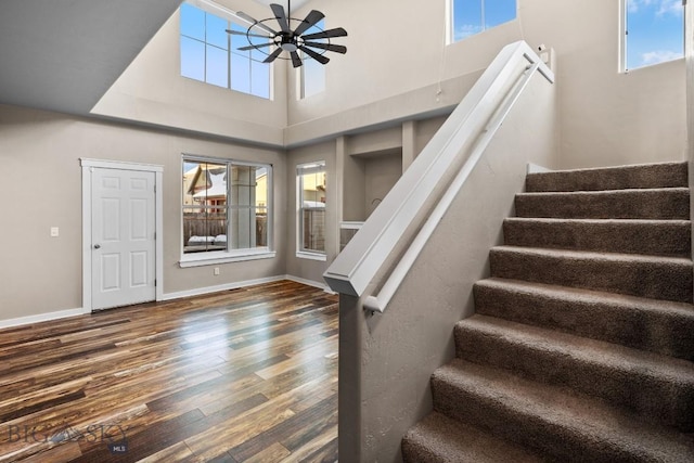 stairway with ceiling fan, hardwood / wood-style floors, and a high ceiling