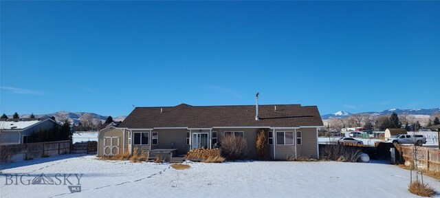 snow covered house featuring an outbuilding, a fenced backyard, a mountain view, and a storage unit