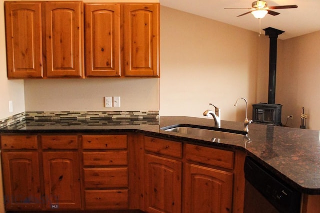 kitchen with brown cabinetry, dark stone counters, a sink, and stainless steel dishwasher