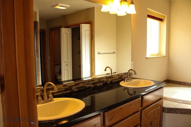 full bath with a chandelier, double vanity, a sink, and a bath