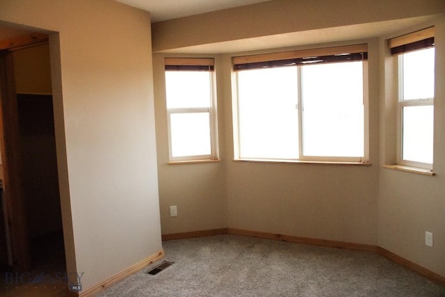 carpeted empty room with a wealth of natural light, visible vents, and baseboards