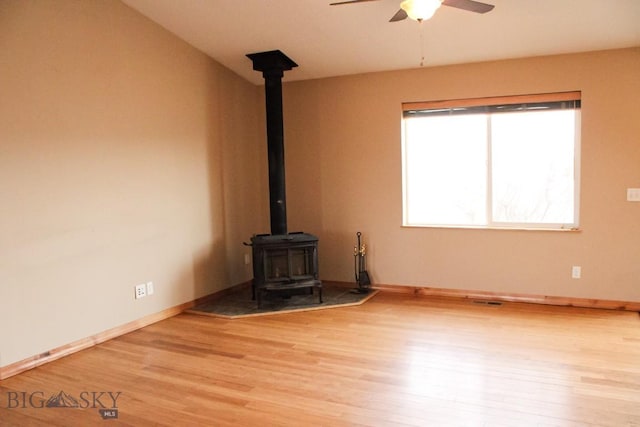 unfurnished living room featuring a wood stove, ceiling fan, baseboards, and wood finished floors