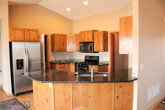 kitchen featuring appliances with stainless steel finishes, dark stone counters, visible vents, and a peninsula