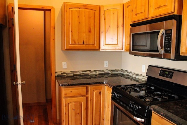 kitchen with stainless steel appliances, wood finished floors, dark stone countertops, and tasteful backsplash