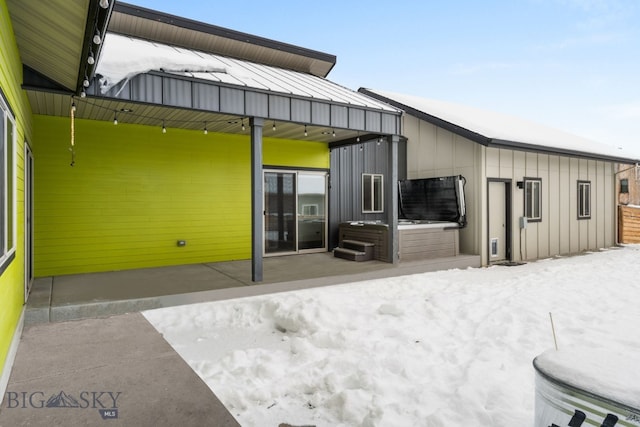 snow covered back of property with a hot tub