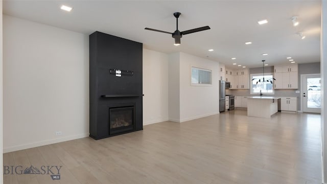 unfurnished living room with ceiling fan, a large fireplace, and light hardwood / wood-style flooring