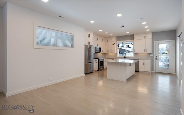 kitchen featuring appliances with stainless steel finishes, decorative light fixtures, a center island, and white cabinets