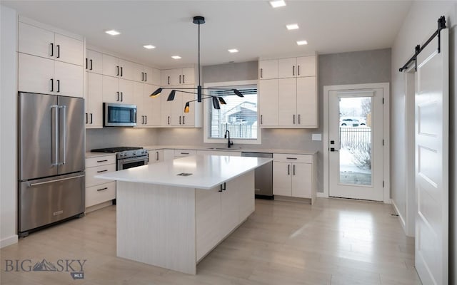 kitchen featuring sink, white cabinetry, premium appliances, decorative light fixtures, and a barn door