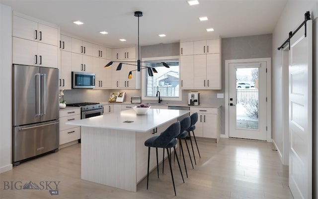 kitchen with pendant lighting, white cabinets, high end appliances, a center island, and a barn door