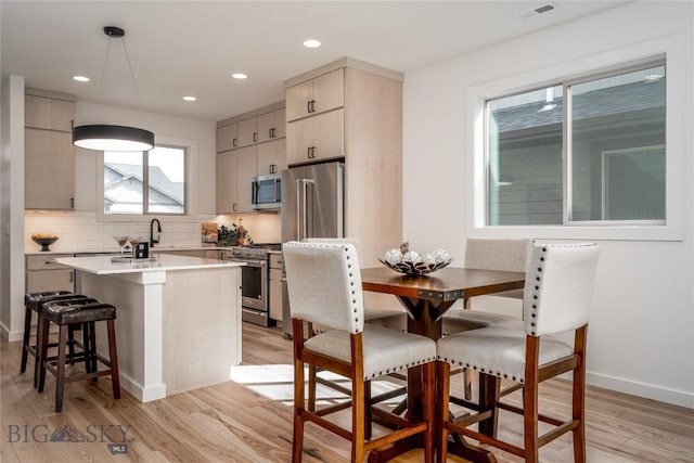 kitchen with tasteful backsplash, decorative light fixtures, a center island, light hardwood / wood-style flooring, and appliances with stainless steel finishes