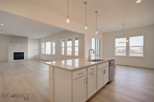 kitchen with white cabinets, dishwasher, sink, hanging light fixtures, and a center island with sink