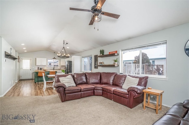 living room featuring light colored carpet, vaulted ceiling, a wealth of natural light, and ceiling fan with notable chandelier