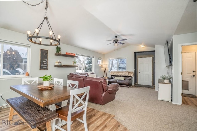 dining space featuring light carpet, vaulted ceiling, and ceiling fan with notable chandelier