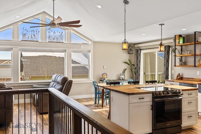 kitchen with butcher block counters, white cabinetry, hanging light fixtures, stainless steel electric stove, and vaulted ceiling