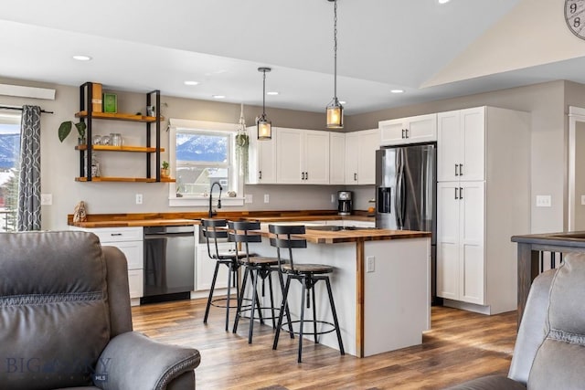 kitchen featuring pendant lighting, white cabinets, a center island, wooden counters, and black dishwasher