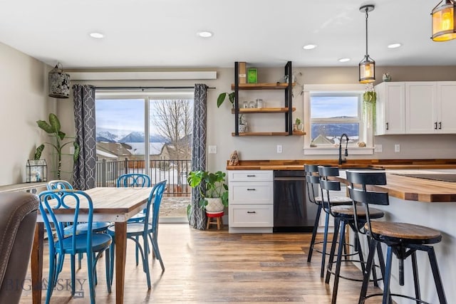 kitchen with decorative light fixtures, white cabinetry, black dishwasher, and wooden counters