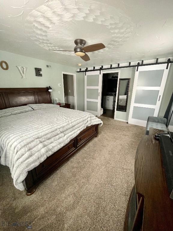 bedroom featuring ceiling fan, a barn door, carpet floors, and a textured ceiling