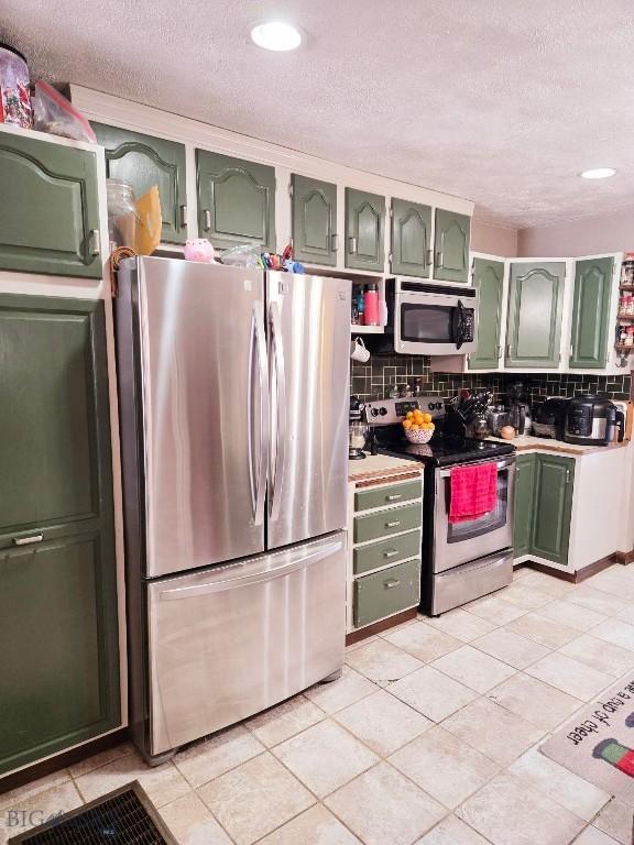 kitchen with appliances with stainless steel finishes, backsplash, light tile patterned floors, a textured ceiling, and green cabinetry