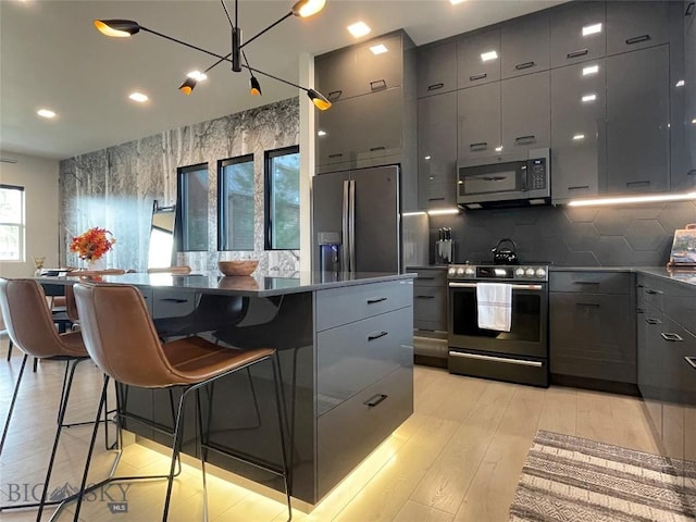 kitchen featuring a breakfast bar, gray cabinetry, stainless steel appliances, modern cabinets, and a center island