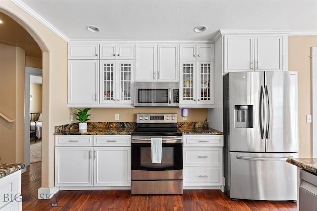 kitchen with dark stone countertops, white cabinetry, appliances with stainless steel finishes, and dark wood-type flooring