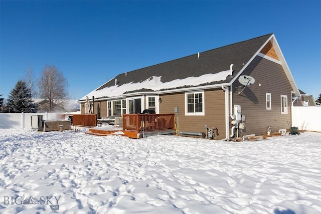 snow covered rear of property with a deck and a hot tub