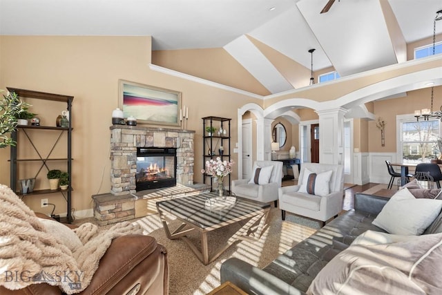 living room featuring decorative columns, ceiling fan with notable chandelier, high vaulted ceiling, and a stone fireplace