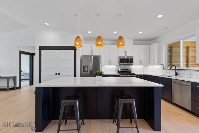 kitchen featuring light stone countertops, a kitchen island, white cabinetry, stainless steel appliances, and sink