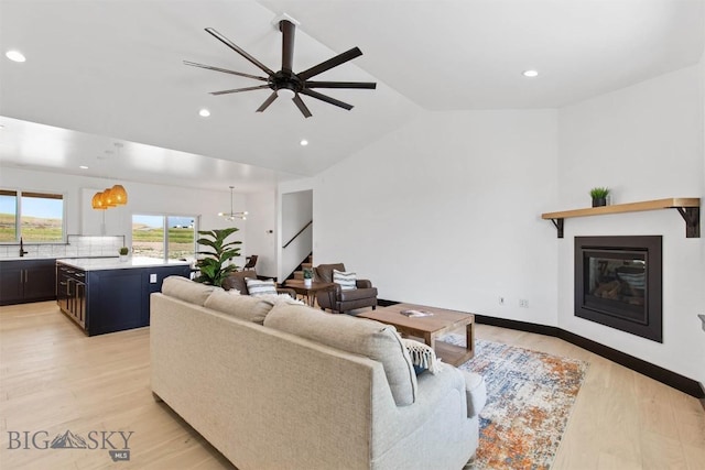 living room featuring light hardwood / wood-style floors, sink, lofted ceiling, and ceiling fan with notable chandelier