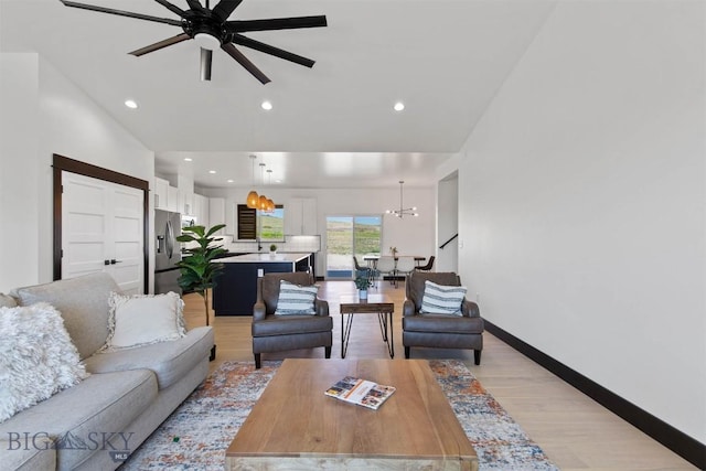 living room with light wood-type flooring and ceiling fan with notable chandelier