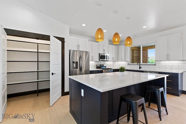 kitchen featuring a kitchen bar, appliances with stainless steel finishes, white cabinetry, a kitchen island, and pendant lighting