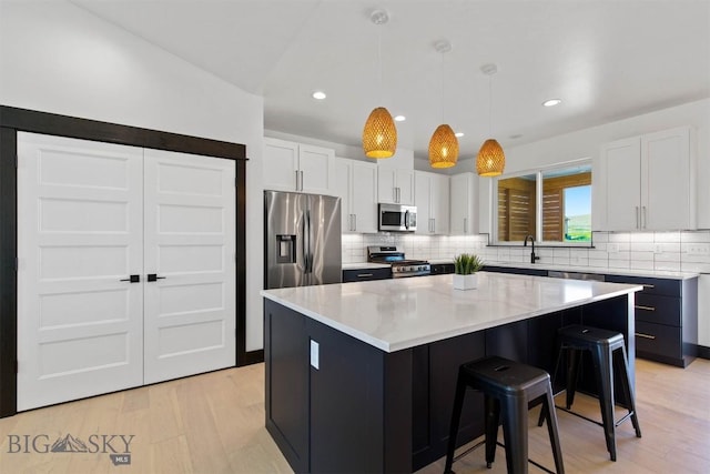 kitchen featuring hanging light fixtures, appliances with stainless steel finishes, white cabinets, a kitchen island, and a breakfast bar area