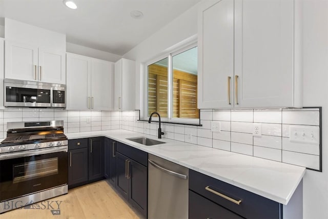 kitchen featuring light stone countertops, white cabinets, stainless steel appliances, decorative backsplash, and sink