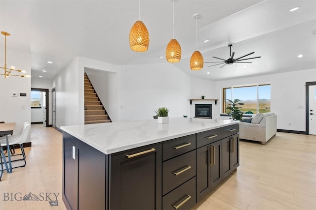 kitchen with decorative light fixtures, light hardwood / wood-style floors, light stone counters, and a center island