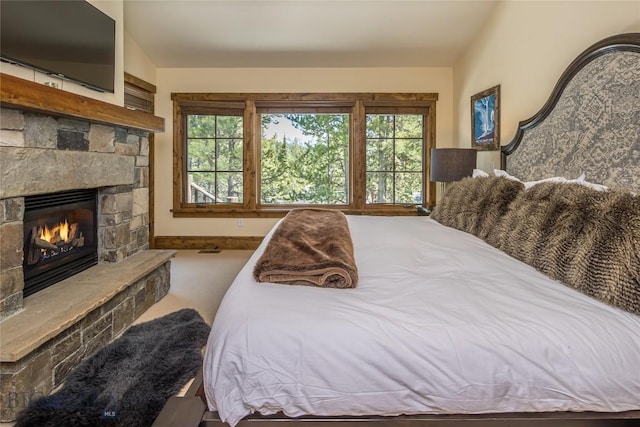 carpeted bedroom featuring vaulted ceiling and a stone fireplace