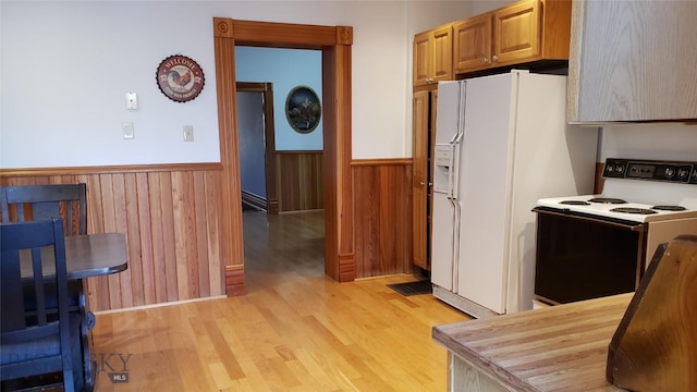 kitchen featuring light wood-type flooring, white fridge with ice dispenser, wooden walls, and electric stove