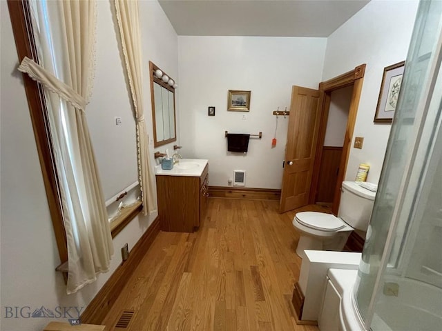 bathroom with wood-type flooring, an enclosed shower, toilet, heating unit, and vanity