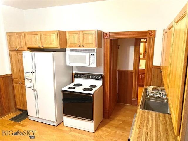 kitchen with sink, light hardwood / wood-style flooring, white appliances, and wooden walls