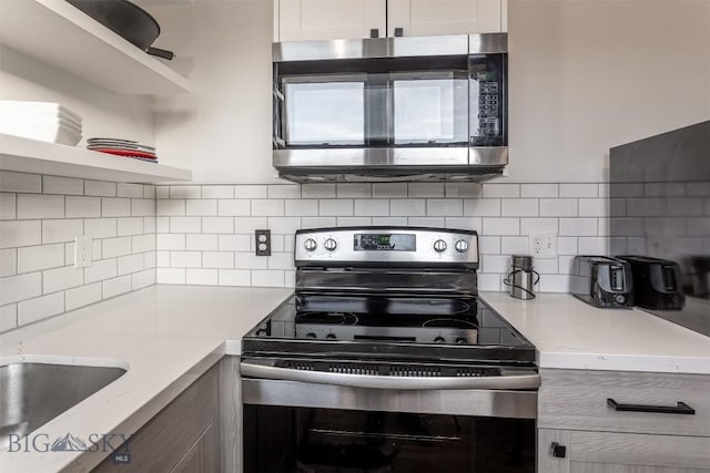 kitchen with tasteful backsplash, white cabinetry, appliances with stainless steel finishes, and light stone counters