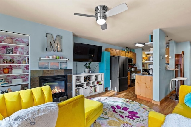 living room with a tiled fireplace, ceiling fan, and light hardwood / wood-style flooring