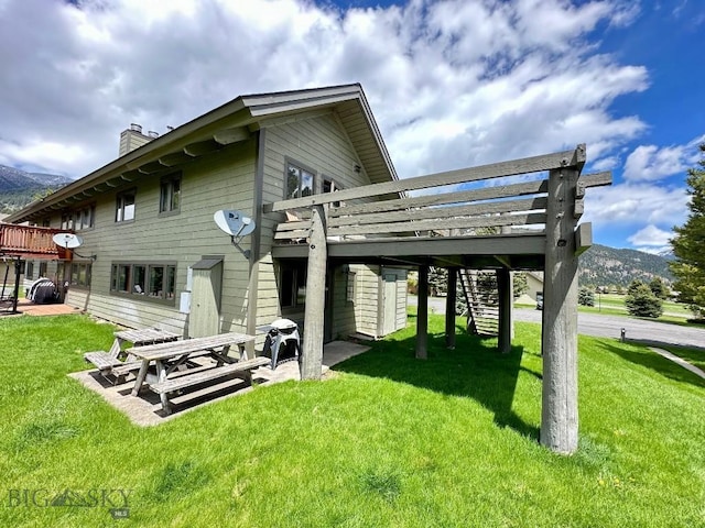 rear view of house with a yard, a deck with mountain view, and a patio area