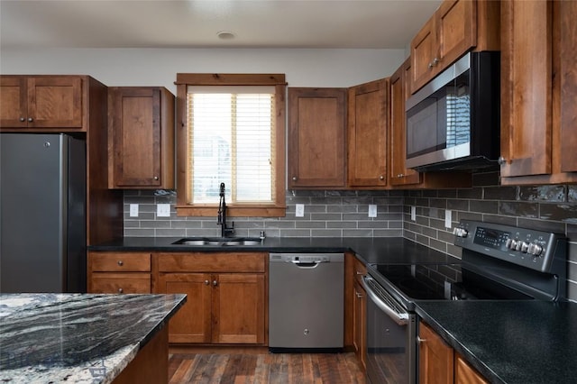 kitchen with appliances with stainless steel finishes, sink, dark stone counters, decorative backsplash, and dark wood-type flooring