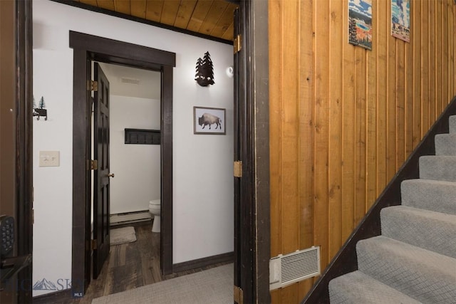 stairway featuring wood-type flooring, a baseboard heating unit, and wood walls