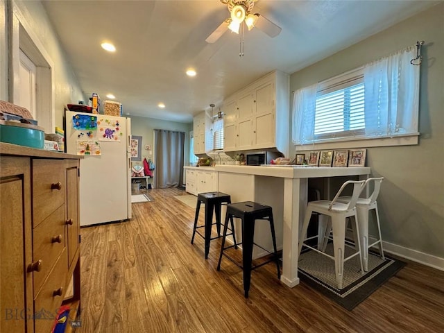 kitchen with a breakfast bar, white cabinetry, white fridge, kitchen peninsula, and light wood-type flooring