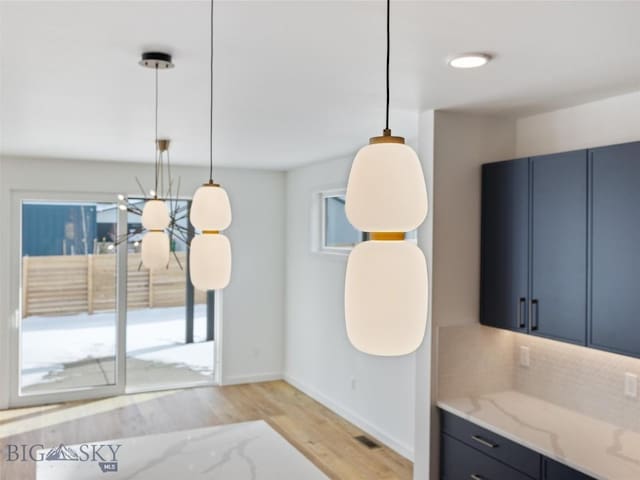 kitchen with hanging light fixtures, light wood-type flooring, blue cabinets, and light stone counters