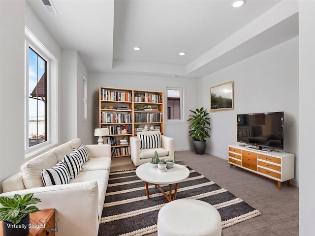 living room featuring plenty of natural light, a raised ceiling, and dark colored carpet