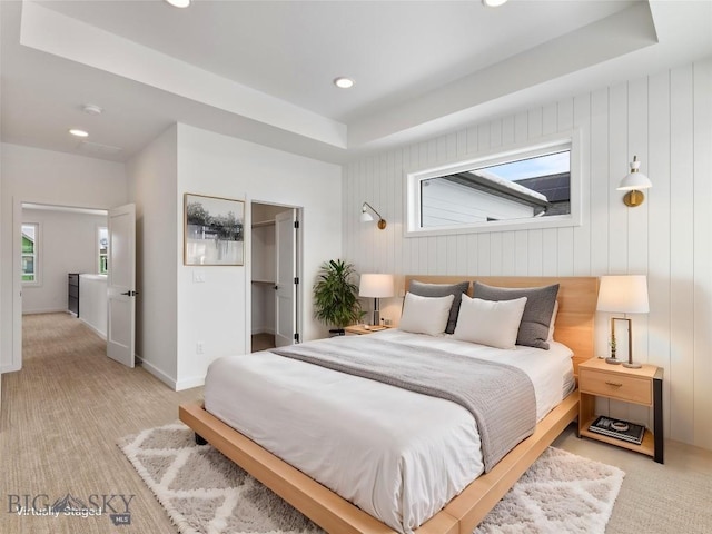 bedroom with light colored carpet, a spacious closet, a raised ceiling, and a closet