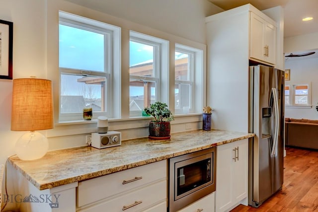 kitchen featuring appliances with stainless steel finishes, light stone countertops, light hardwood / wood-style flooring, and white cabinets