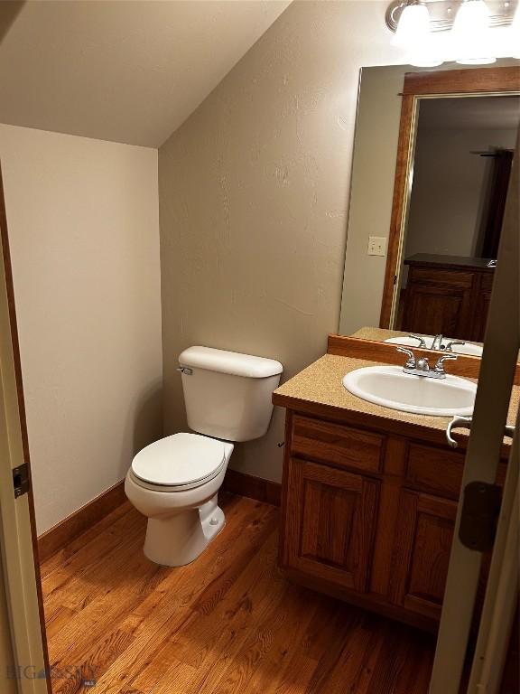 bathroom featuring wood-type flooring, vaulted ceiling, vanity, and toilet