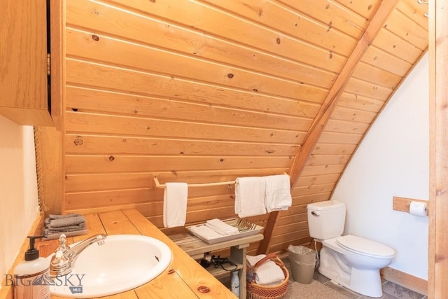 bathroom with toilet, sink, vaulted ceiling with beams, wood walls, and wooden ceiling