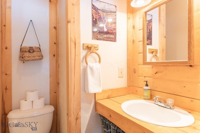 bathroom with wooden walls, toilet, and sink